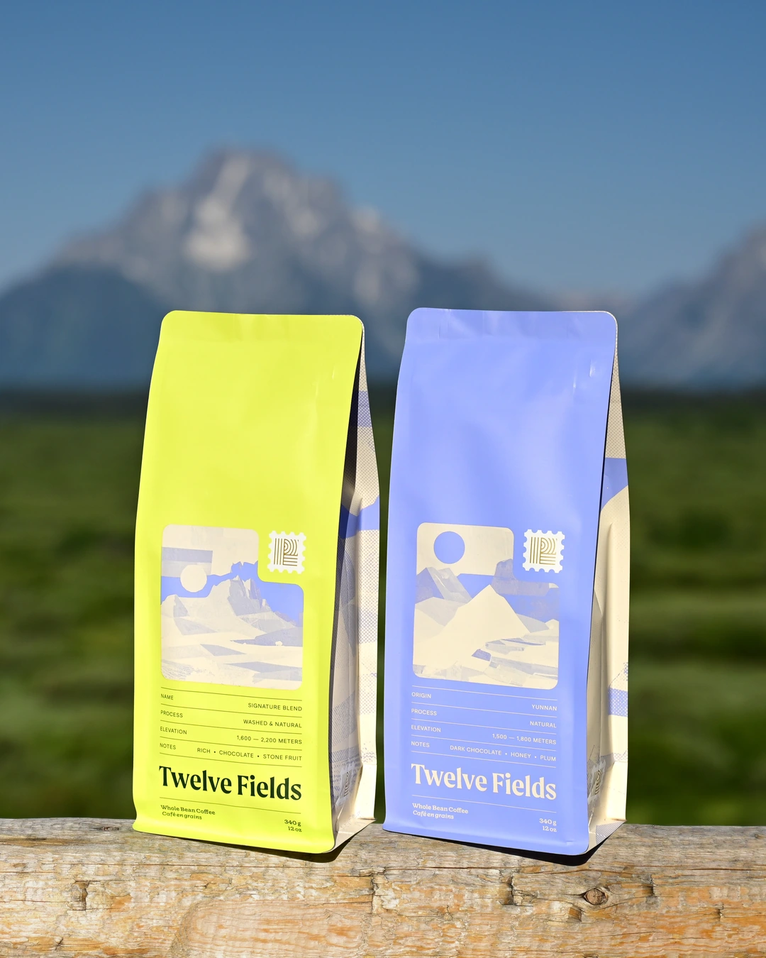 Signature Blend and Yunnan Natural coffee bags together on a log against the Montana mountains