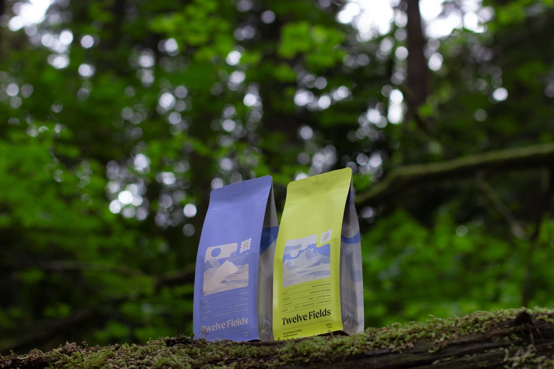 Two Twelve Fields coffee bags displayed on a mossy log in the forest